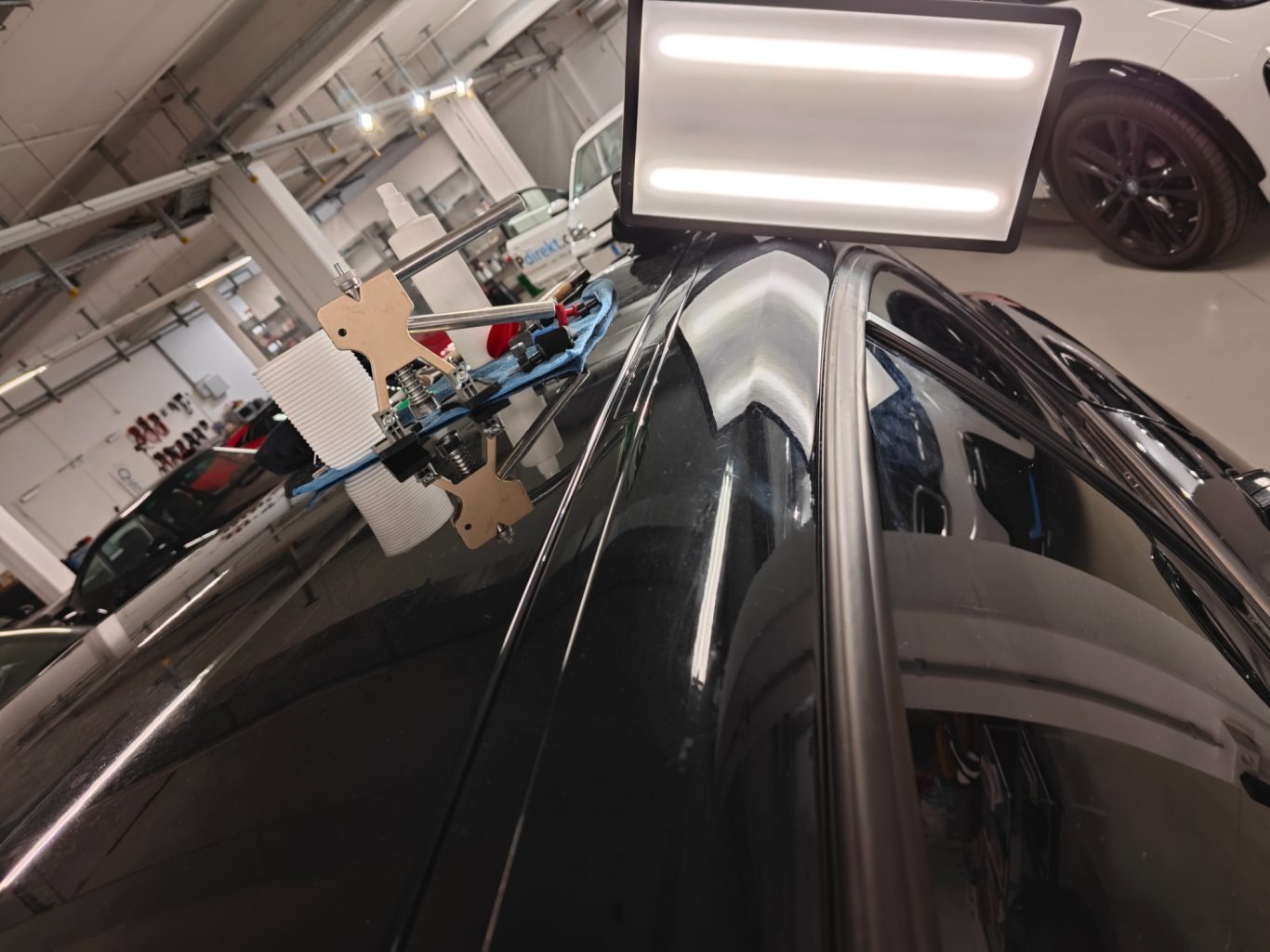 BMW 1er Dachholm nachher Ein schwarzes Auto, teilweise in einer Werkstatt, mit einem Monitor im Vordergrund.