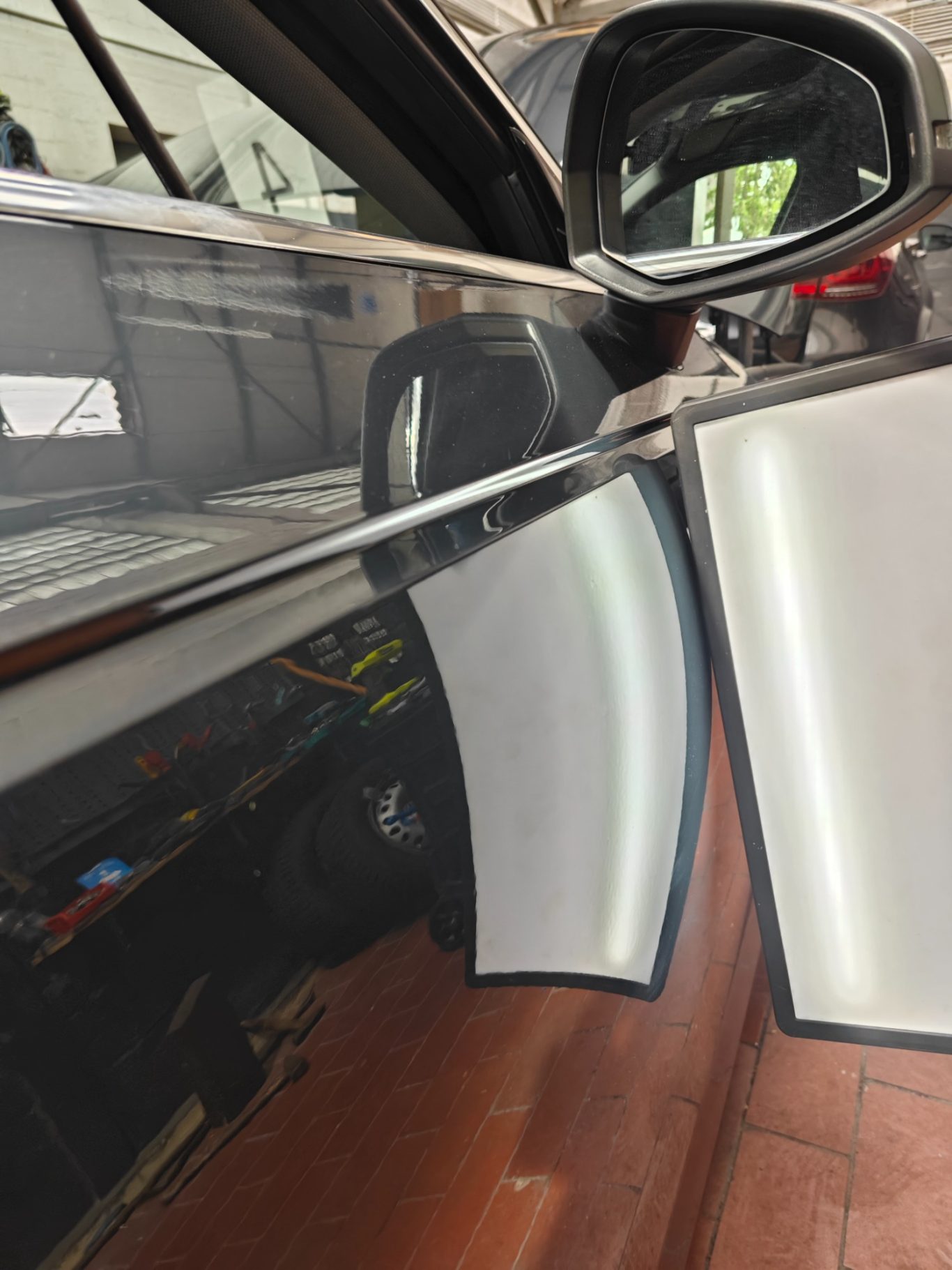 Audi A4 Türe nachher Reflexion auf einer schwarzen Autoscheinwerferverkleidung, Handwerker im Hintergrund.