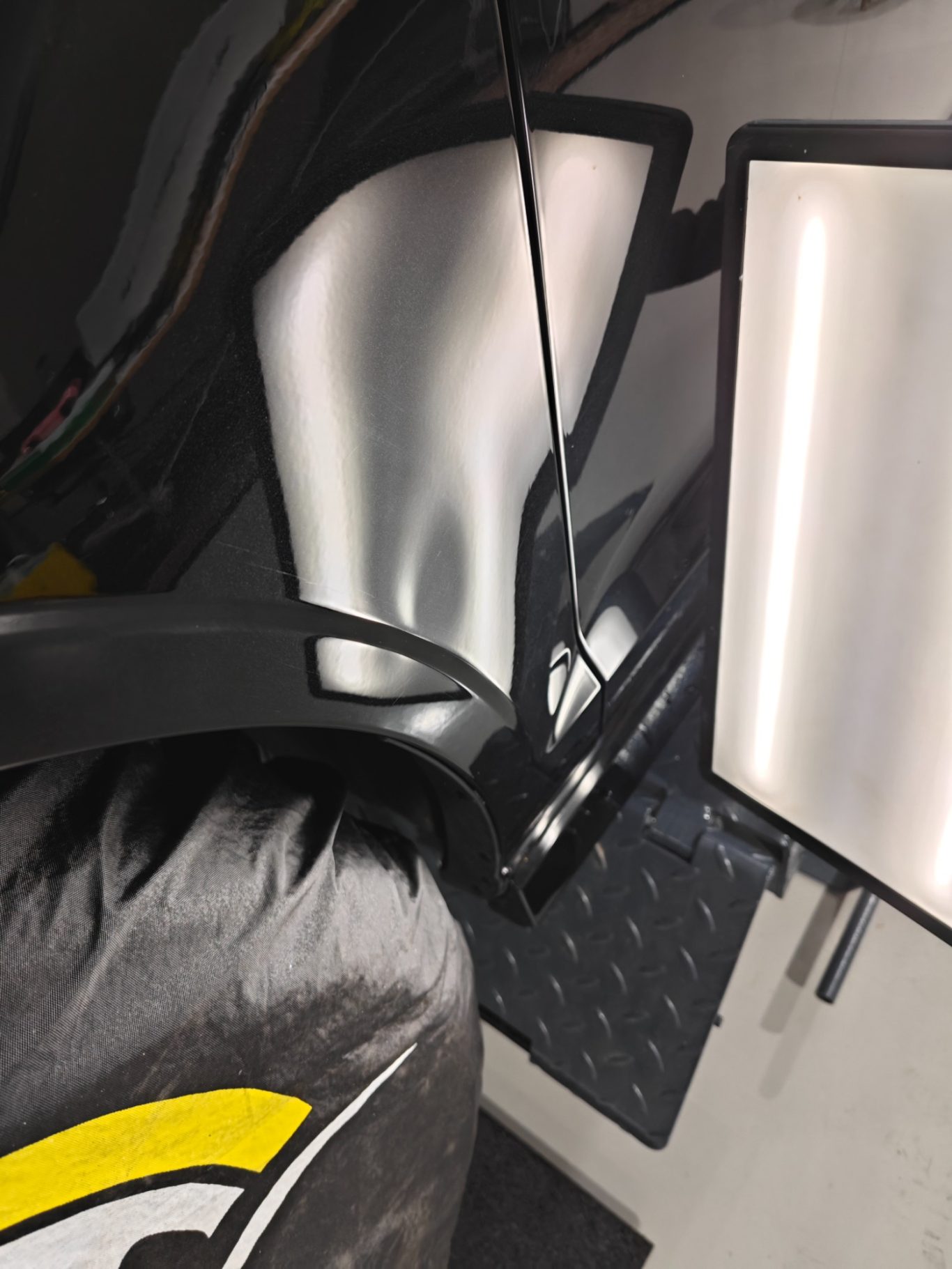 Audi RS3 Kotflügel vorher Reflektierende Oberflächen eines schwarzen Autos neben zwei Lichtquellen.