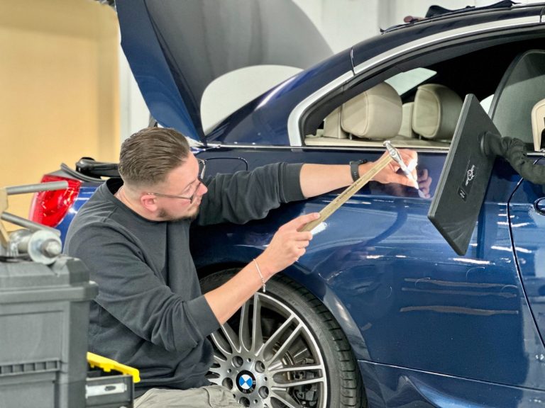 Ein Mann arbeitet an der Karosserie eines blauen BMW 
